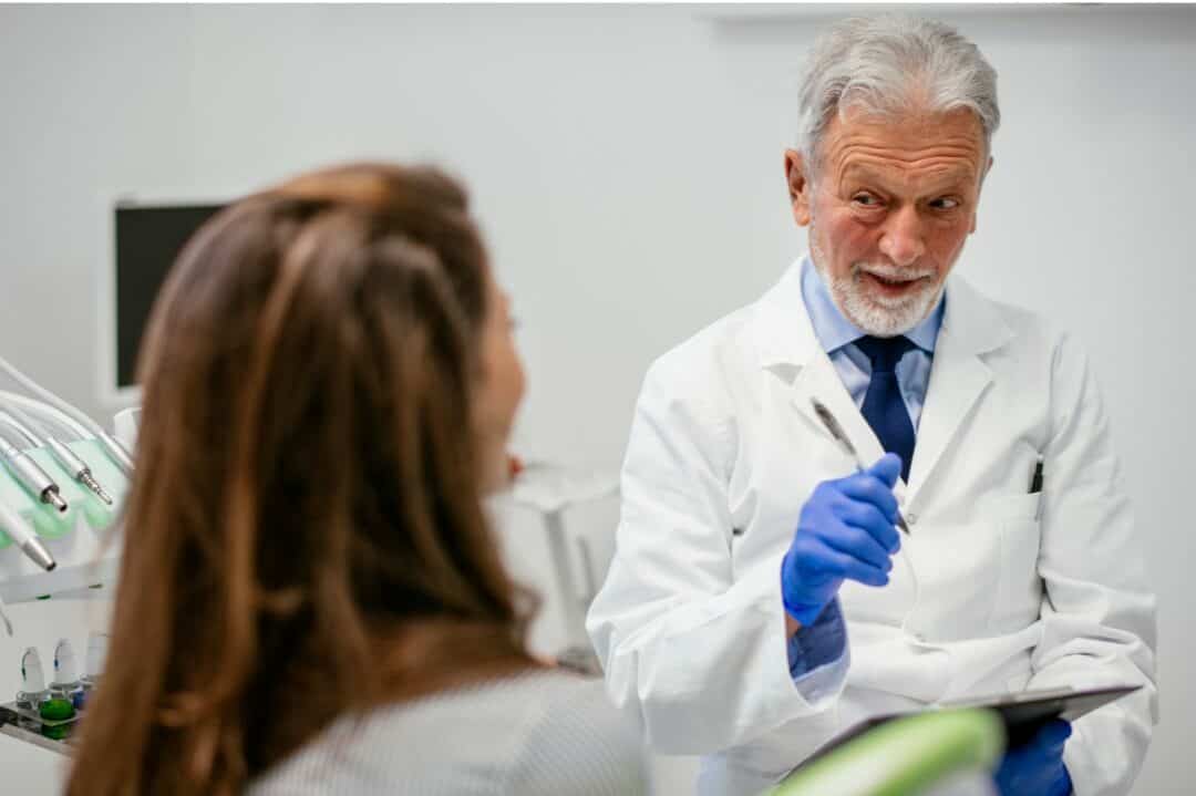 Older Dentist talking to female patient