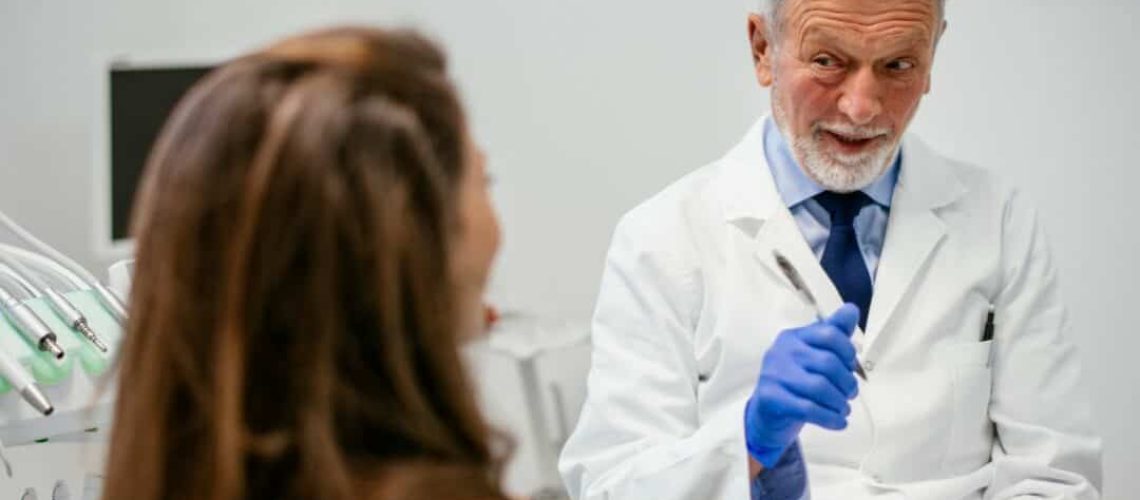 Older Dentist talking to female patient